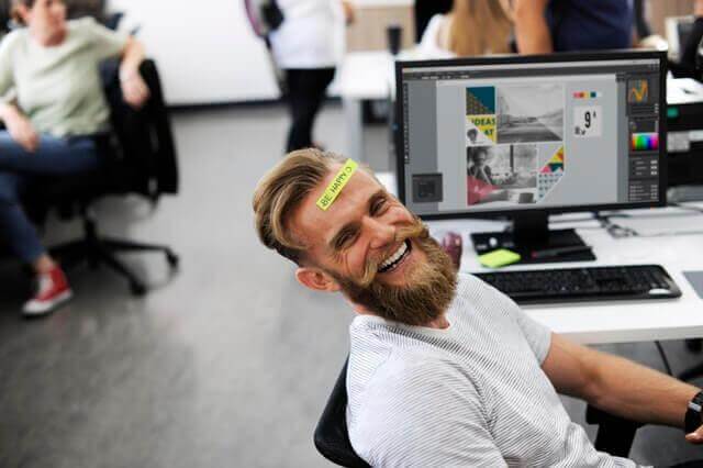 Ein Mann im Büro hat ein Post-it auf der Stirn und lacht. 