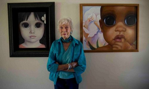 Margaret Keane steht vor ihren Werken.