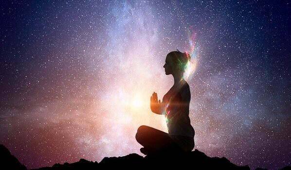 Eine Frau meditiert unter dem freien Sternenhimmel. 
