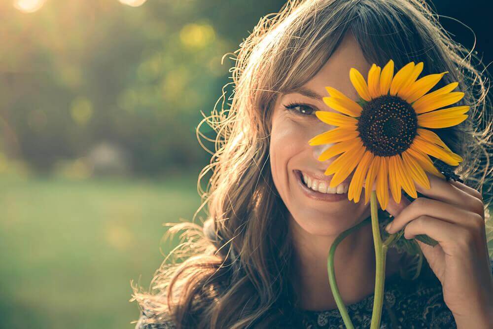 Lachende Frau hält sich eine Sonnenblume vors Gesicht