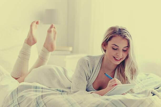 Frau liegt in ihrem Bett und schreibt in ihr Tagebuch