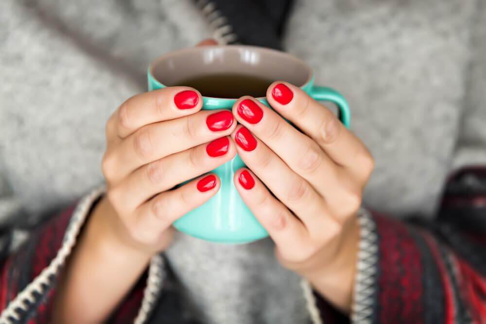 Frau mit roten Fingernägeln hält eine mintgrüne Tasse 