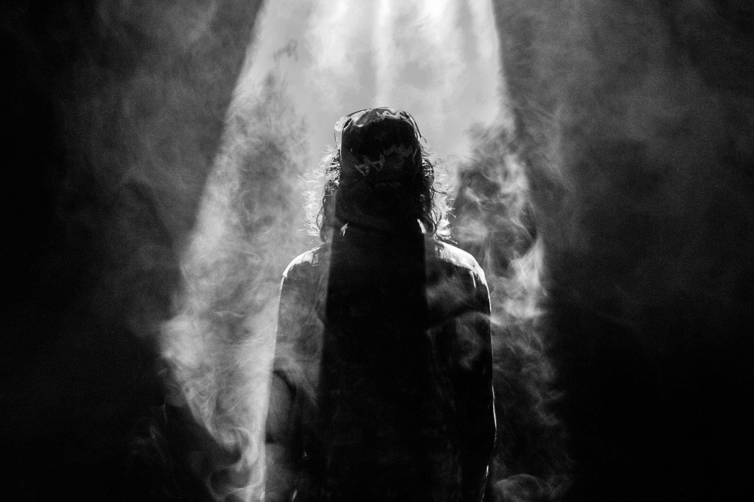 Mann steht mit Rücken im Lichtstrahl und ist umgeben von Dunkelheit