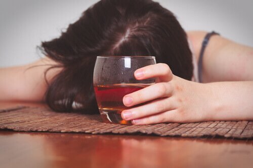 Eine Frau ist mit einem Whiskeyglass in der Hand auf der Tischplatte eingeschlafen. 