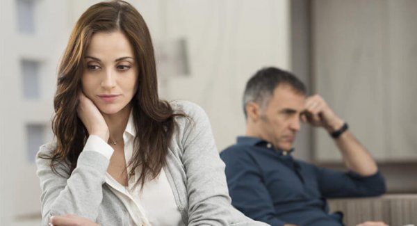 Besorgte Frau schaut nach unten, ihr Partner im Hintergrund