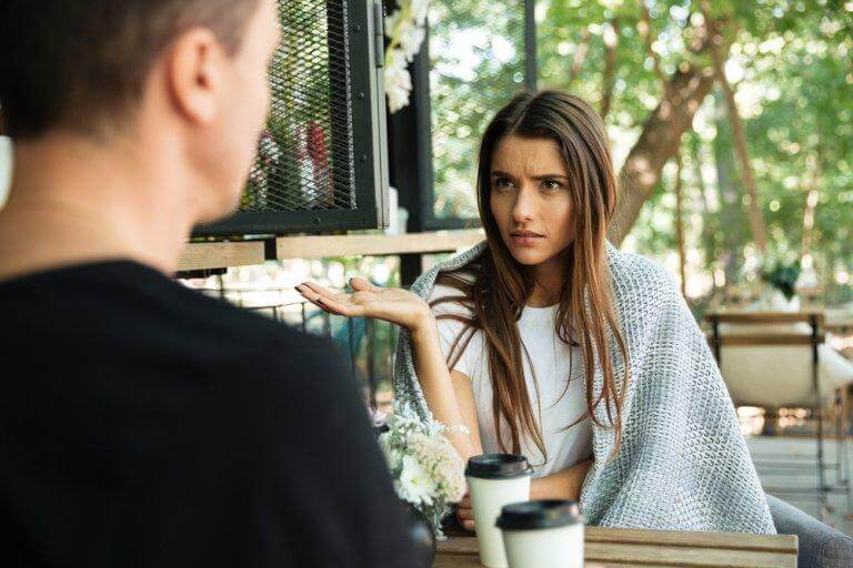 Eine Frau argumentiert, ihr Partner sitzt gegenüber und hört zu. Wie kann man Kommunikationsfehler vermeiden?