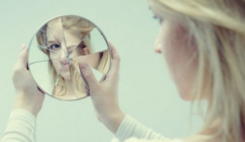 Frau schaut in einen zerbrochenen Spiegel als Symbol für die Fallen des Egos