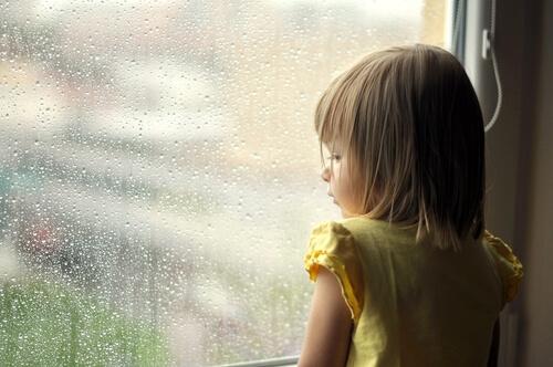 Kleines Mädchen schaut nachdenklich aus einem Fenster
