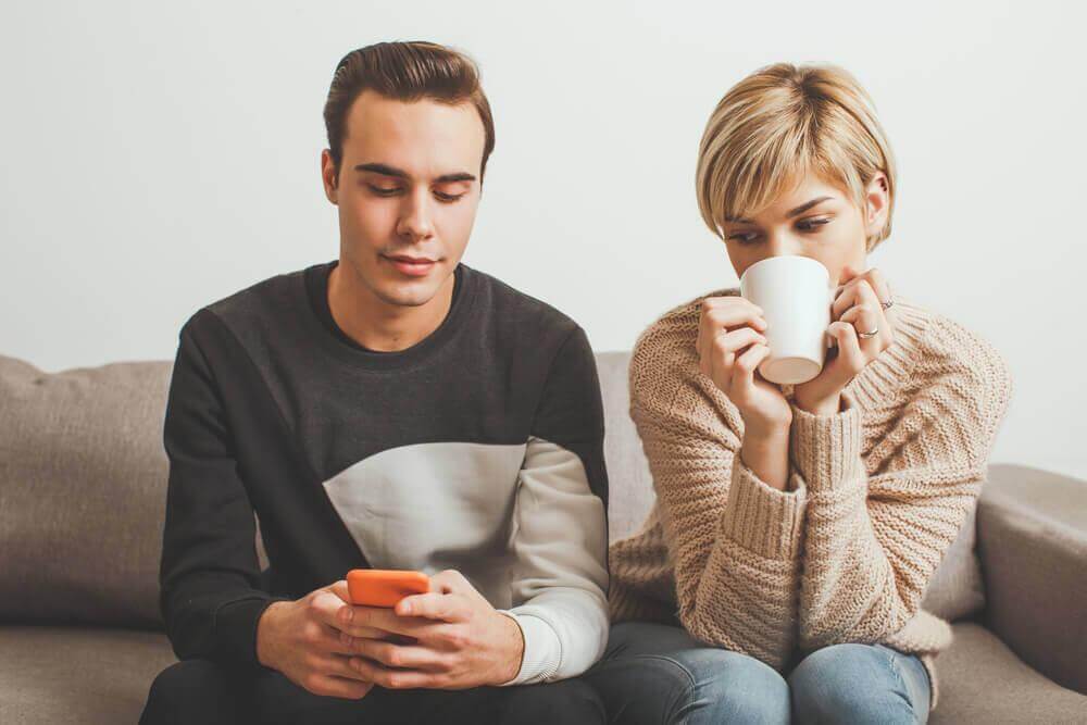 Frau schaut ihrem Partner über die Schulter auf sein Handy