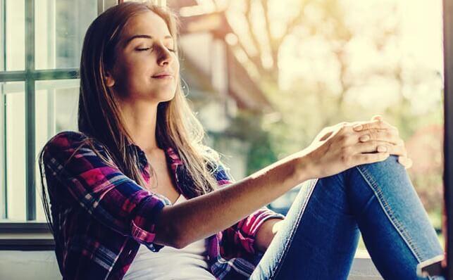 Lächelnde Frau sitzt mit geschlossenen Augen am Fenster