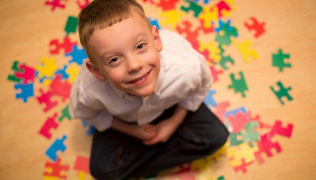 Lachender Junge mit Autismus umgeben von Puzzleteilen