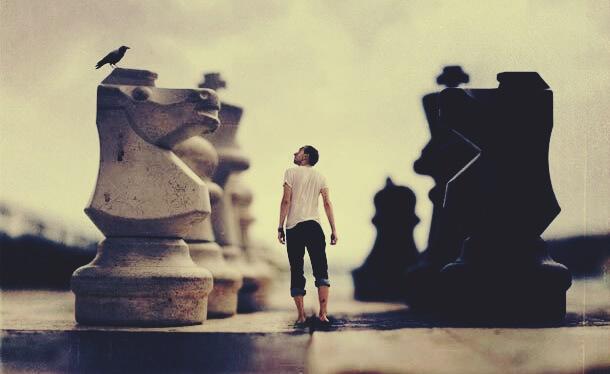 Mann steht auf einem Schachbrett neben Schachfiguren
