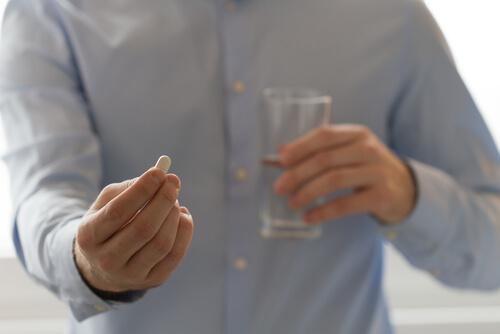 Mann mit einer Tablette und einem Glas Wasser in der Hand