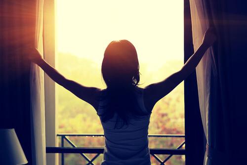 Eine Frau zieht ihre Fenstervorhänge zur Seite, um den Morgen zu begrüßen.