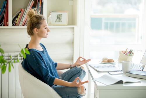 Frau meditiert auf einem Stuhl an ihrem Schreibtisch