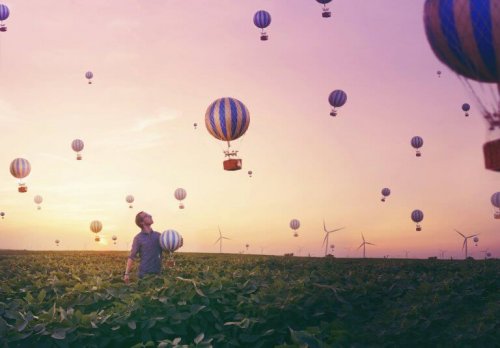 Ein Mann steht in einem Feld und beobachtet Heißluftballons.