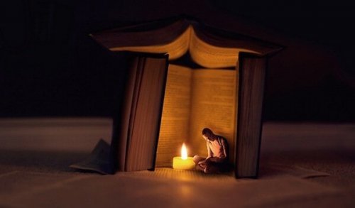 Ein Mann sitzt in der Dunkelheit in einem Zelt aus Büchern vor einer Kerze. 