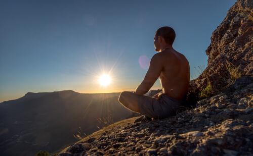 Mann meditiert auf einem Berg bei Sonnenaufgang
