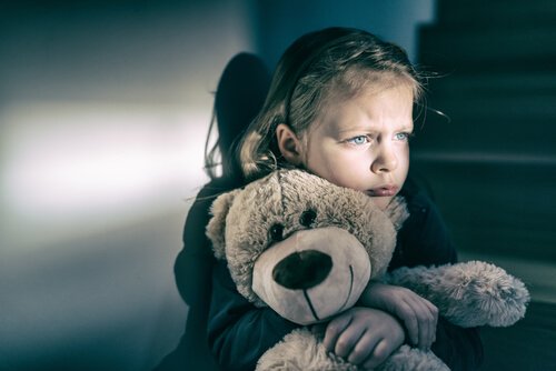 Trauriges Mädchen, das mit einem Teddybär kuschelt