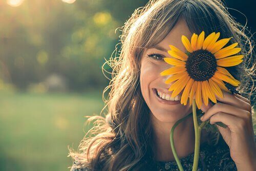Eine Frau hält sich eine Sonnenblume vors Gesicht.