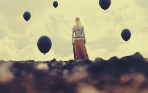 Eine blonde Frau steht auf einem Feld und ist von dunklen Luftballons umgeben. 