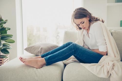 Frau sitzt mit Bauchschmerzen auf der Couch