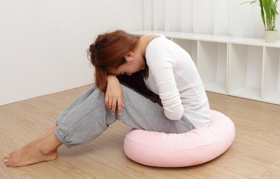 Frau sitzt zusammengekauert mit Schmerzen auf dem Boden