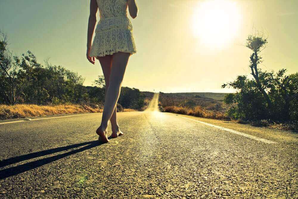 Frau spaziert ohne Schuhe eine Straße entlang