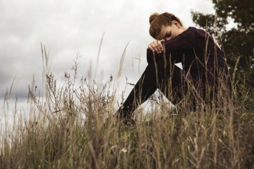 Eine junge Frau sitzt traurig an einem Flussufer und hat ihren Kopf auf die Knie gelegt. 