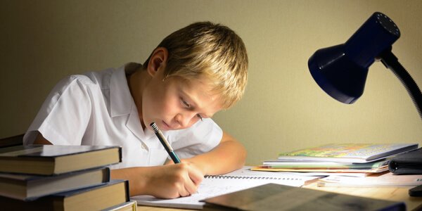 Ein Junge sitzt an seinen Hausaufgaben im Schein einer Schreibtischlampe. 