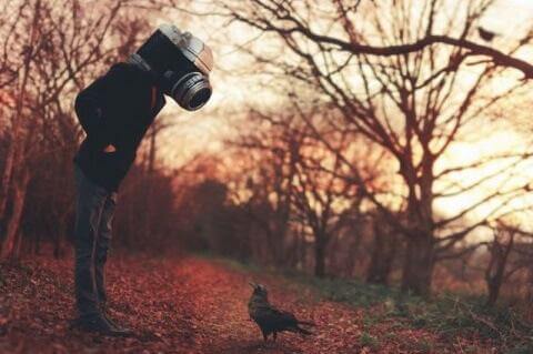 Mann mit einer Kamera als Kopf schaut auf einen Vogel