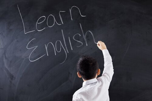 Ein Junge schreibt "Learn English" an die Tafel.