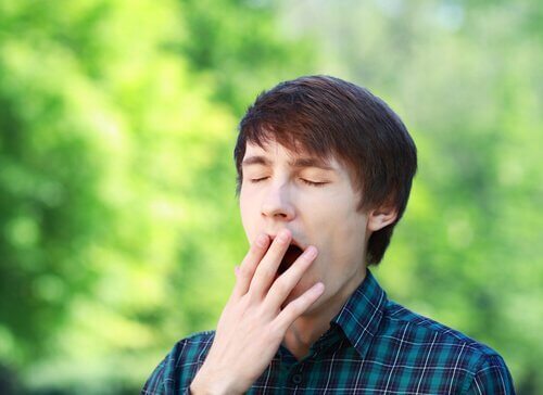Ein junger Mann hält sich die Hand vor den Mund, weil er gähnen muss. 