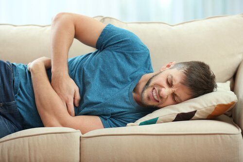 Mann liegt mit Bauchschmerzen auf dem Sofa.