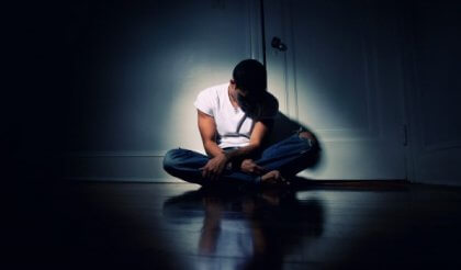 Ein Teenager sitzt traurig in einer dunklen Ecke. 