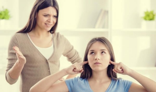 Ein Teenager steckt sich die Finger in die Ohren, während seine Mutter mit ihm schimpft. 
