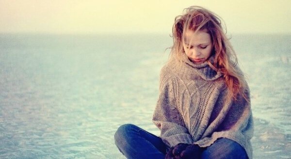 Ein Mädchen sitzt traurig und in Gedanken versunken am Meer.