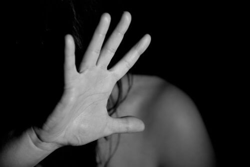 Eine junge Frau hält ihre Hand vor ihr Gesicht, um sich zu schützen.