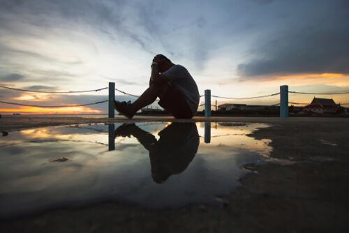 Mann sitzt zusammengekauert am Wasser