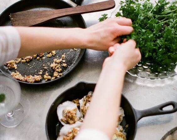Hände bereiten ein Essen zu und benutzen dazu Kräuter aus einer Schüssel. 