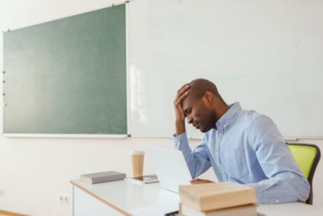 Erschöpfter Lehrer sitzt im Klassenraum.