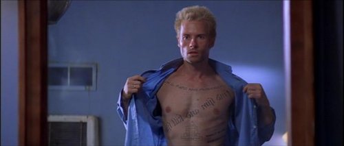 Filmcharakter aus "Memento", der sein Shirt öffnet und seine Tattoos zeigt.