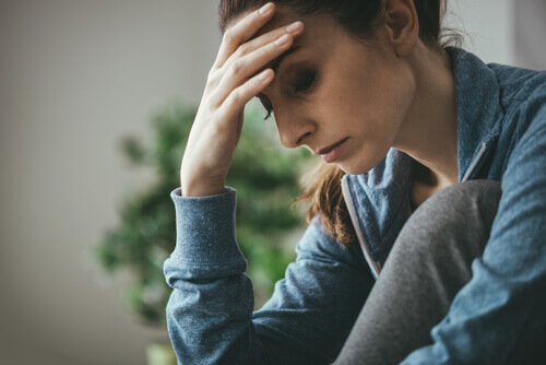 Eine Frau sitzt erschöpft an einem Tisch und stützt ihren Kopf mit einer Hand ab.