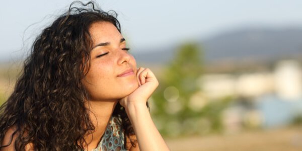 Eine Frau genießt die Sonnenstrahlen und hat ihre Augen dabei geschlossen. 