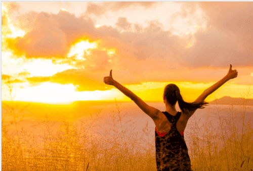 Eine Frau begrüßt glücklich den Sonnenaufgang.