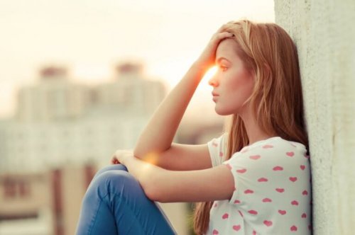 Eine Frau sitzt nachdenklich an einer Mauer, während die Sonne im Hintergrund untergeht.