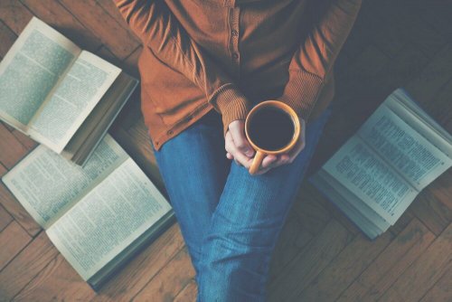 Eine Frau sitzt mit einem Kaffee und um sie liegen ein paar Bücher.