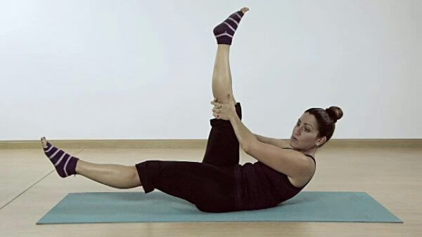 Eine Frau liegt auf einer Yogamatte und macht Pilates. 