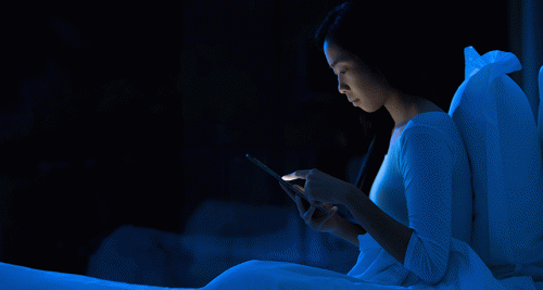 Eine junge Frau tippt nachts im Bett auf ihrem Handy rum.