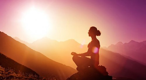 Eine Frau meditiert im Sonnenuntergang vor einer Bergkulisse.